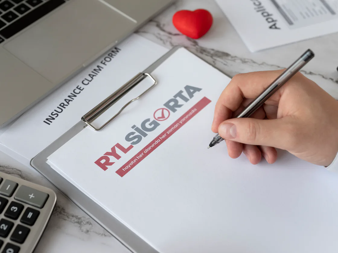 An insurance claim form with the RYL Sigorta logo, being filled in by hand at a desk